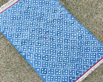 May include: A blue and white patterned rug with a diamond design. The rug has a fringe border and is made of a soft, woven material.
