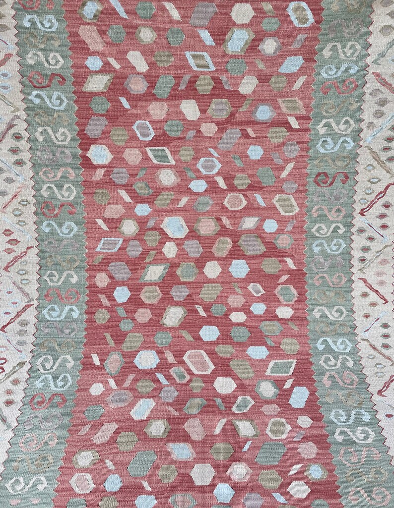 K&ouml;nnte beinhalten: Ein roter, gr&uuml;ner und wei&szlig;er Teppich mit geometrischem Muster. Der Teppich hat einen Rand mit einem sich wiederholenden Muster aus Spiralen.