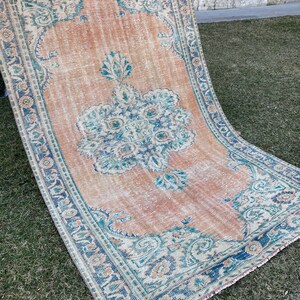 May include: A vintage rug with a faded peach background and a blue and green floral pattern. The rug has a fringed edge.