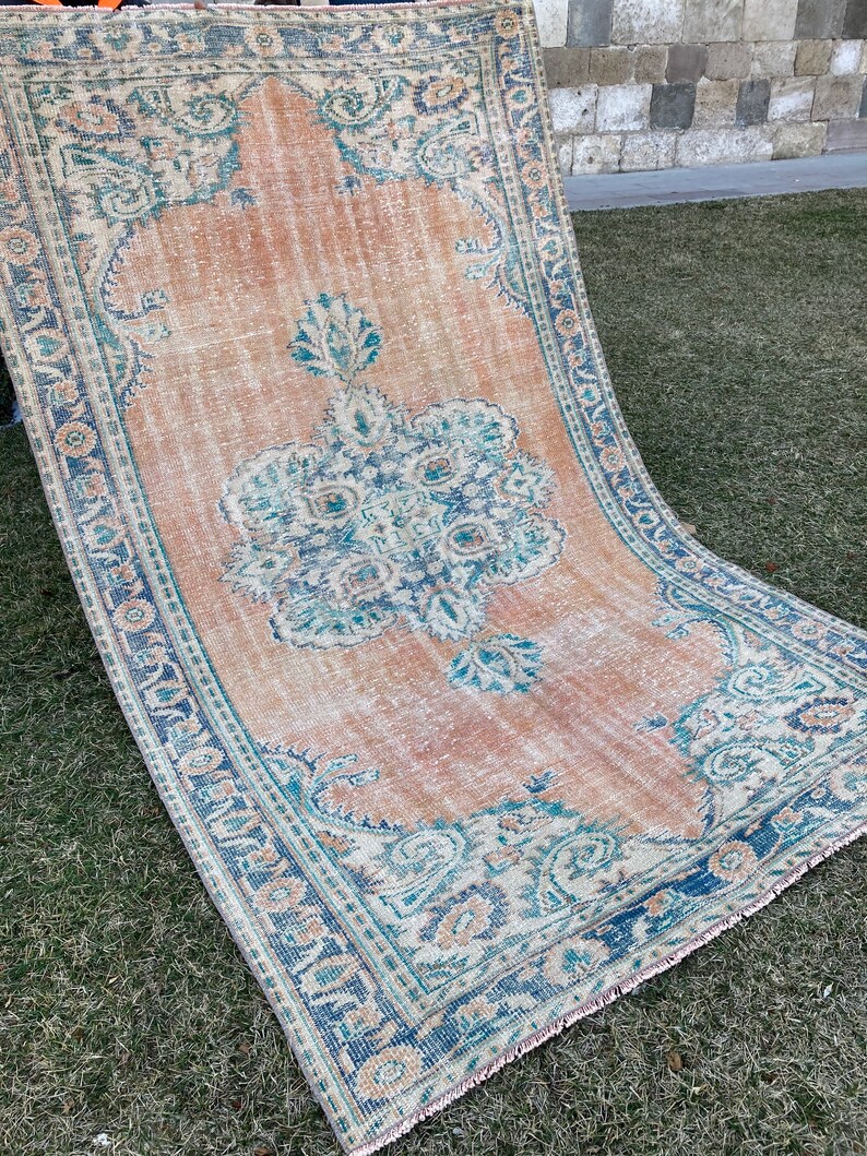 May include: A vintage rug with a faded peach background and a blue and green floral pattern. The rug has a fringed edge.
