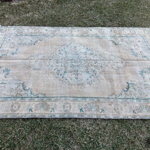 May include: A vintage rug with a light beige background and a faded blue and brown floral pattern. The rug has a distressed look and a fringed edge.