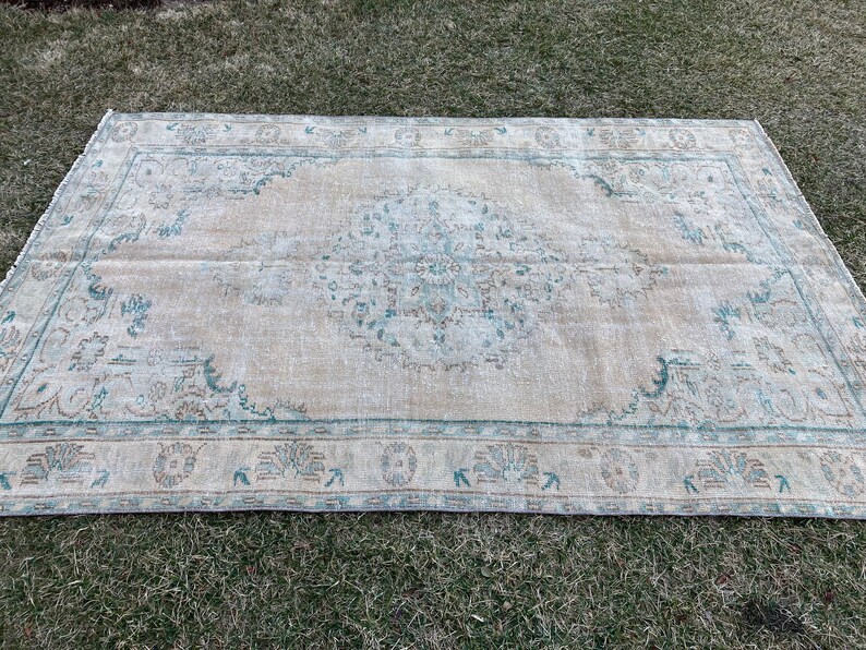 May include: A vintage rug with a light beige background and a faded blue and brown floral pattern. The rug has a distressed look and a fringed edge.