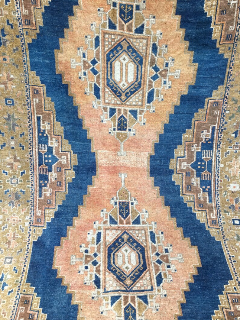 May include: A vintage rug with a blue and orange geometric pattern. The rug has a central medallion with a repeating design of diamonds and squares.