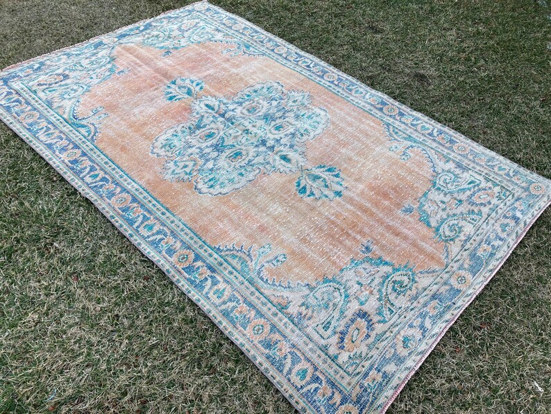 May include: A vintage rug with a light peach background and a blue and white floral pattern. The rug has a faded, distressed look, giving it a unique and charming character.