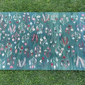 May include: A teal blue rug with a floral pattern. The flowers are white, pink, and red. The rug has a fringe border.