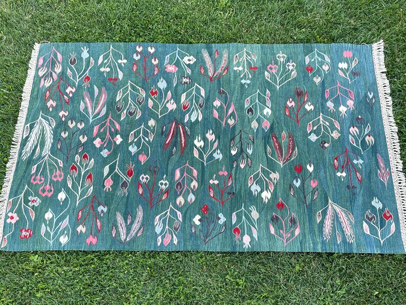 May include: A teal blue rug with a floral pattern. The flowers are white, pink, and red. The rug has a fringe border.