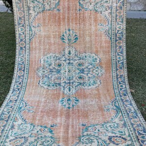 May include: A vintage rug with a faded peach background and a blue and white floral pattern. The rug has a fringed edge.