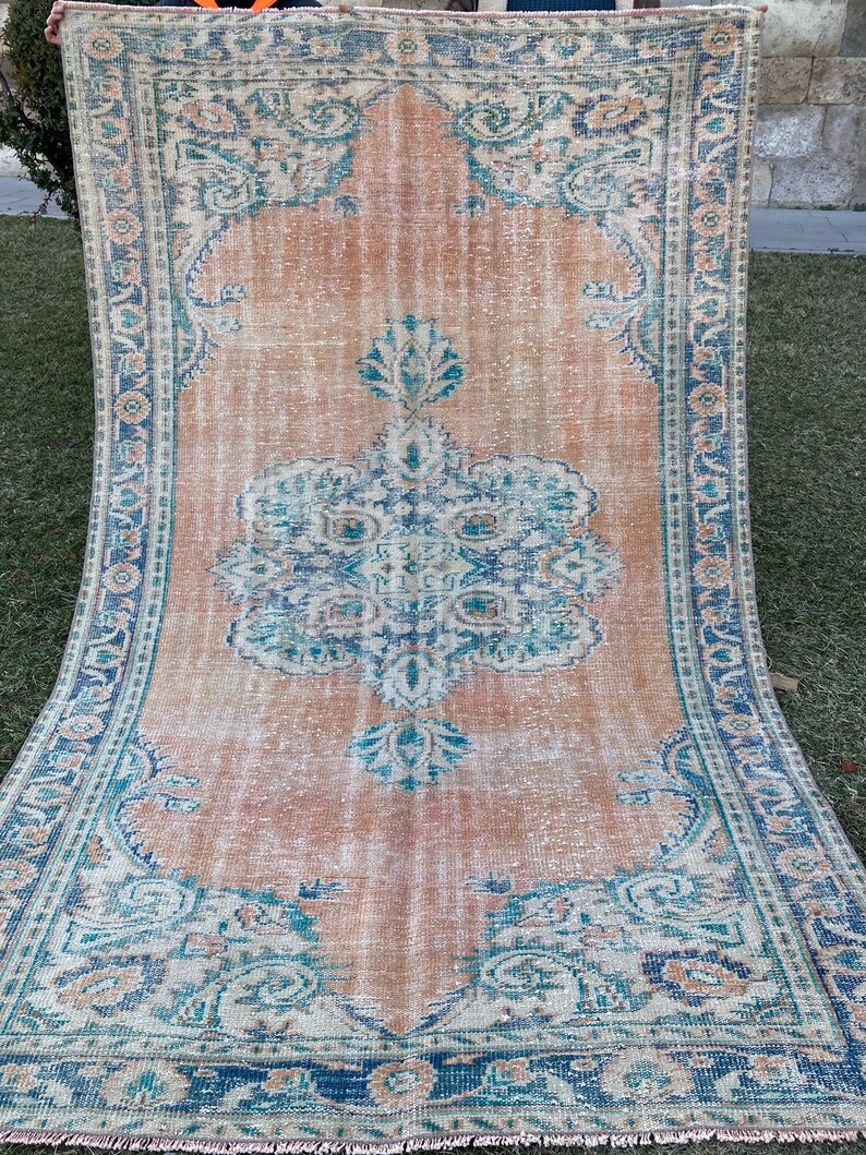 May include: A vintage rug with a faded peach background and a blue and white floral pattern. The rug has a fringed edge.