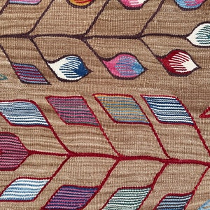 May include: A close-up of a woven fabric with a geometric pattern. The pattern features red, blue, pink, and yellow colors. The fabric has a brown background.