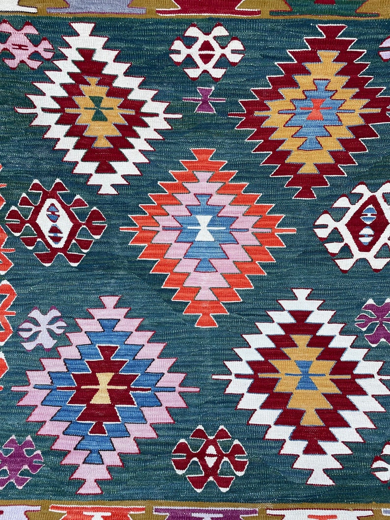 May include: A traditional Turkish rug with a geometric pattern in shades of red, blue, white, and green. The rug features a repeating design of diamonds and squares.