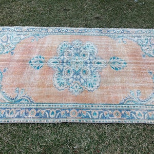 May include: A vintage rug with a faded peach background and a blue and white floral pattern. The rug has a distressed look and a fringed edge.