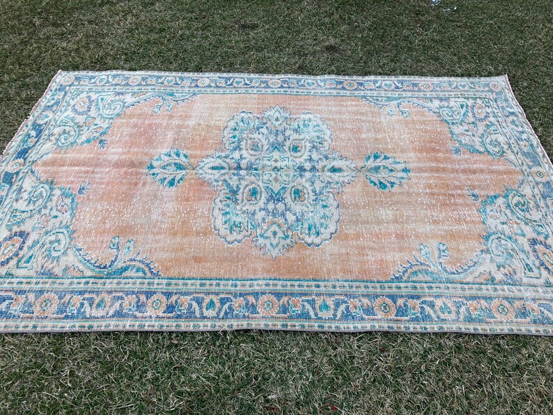 May include: A vintage rug with a faded peach background and a blue and white floral pattern. The rug has a distressed look and a fringed edge.