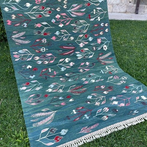 May include: A teal blue rug with a floral pattern featuring white, pink, and red stylized flowers and leaves. The rug has a fringe border.
