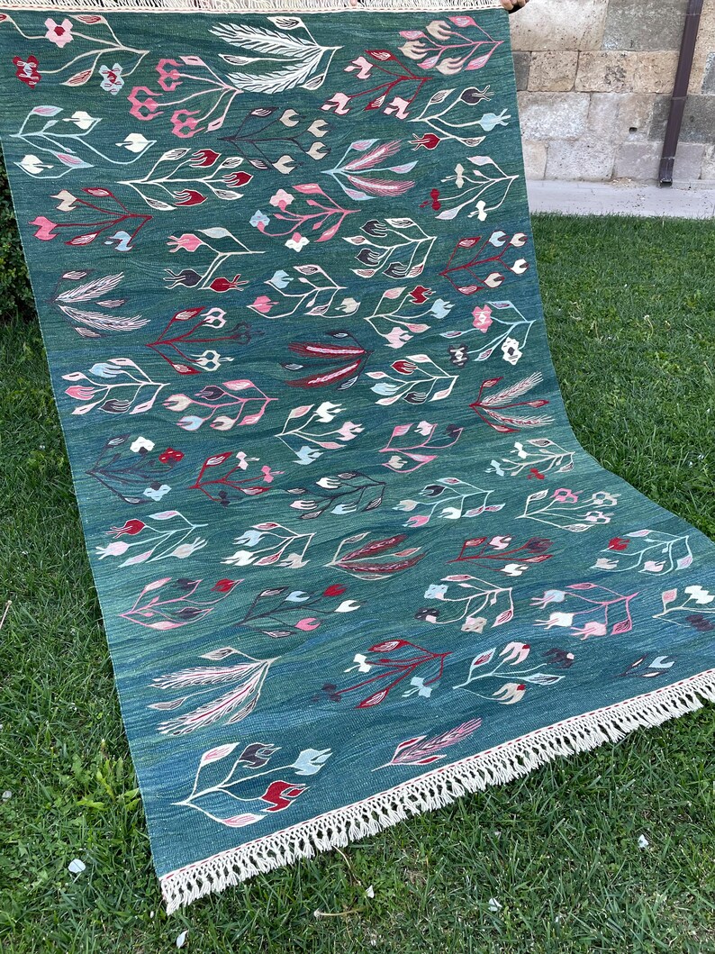 May include: A teal blue rug with a floral pattern featuring white, pink, and red stylized flowers and leaves. The rug has a fringe border.