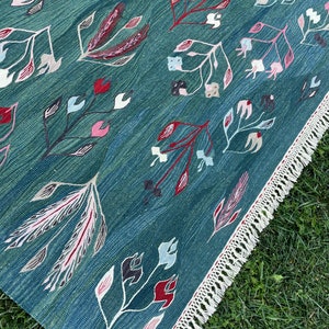 May include: A teal blue rug with a floral pattern in shades of pink, red, and white. The rug has a fringe border.