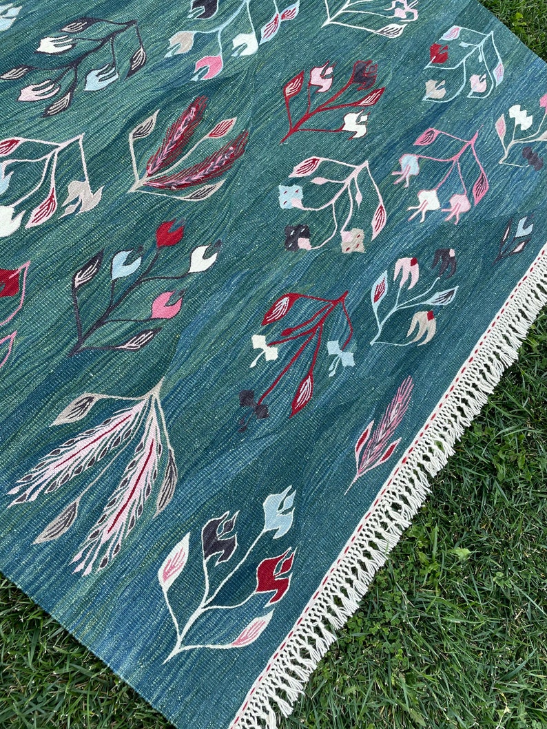 May include: A teal blue rug with a floral pattern in shades of pink, red, and white. The rug has a fringe border.