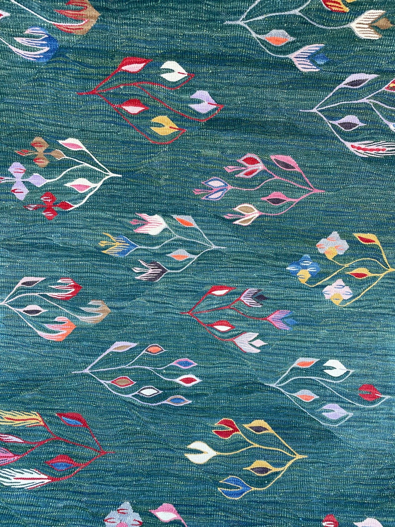 May include: A teal blue fabric with a repeating pattern of stylized flowers in shades of red, pink, yellow, blue, white, and brown.