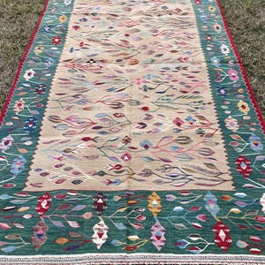 May include: A traditional Turkish rug with a beige background and a green border. The rug features a floral pattern with colourful leaves and flowers.