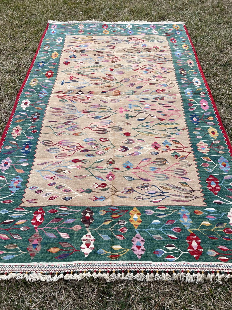 May include: A traditional Turkish rug with a beige background and a green border. The rug features a floral pattern with colourful leaves and flowers.