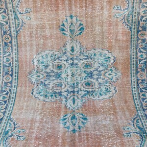 May include: A vintage rug with a faded, light brown background and a central medallion design in shades of blue and white. The rug has a distressed, worn look with a subtle floral pattern.