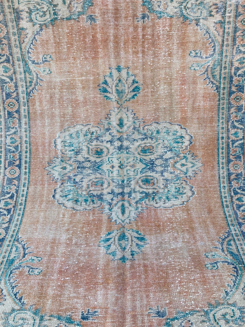 May include: A vintage rug with a faded, light brown background and a central medallion design in shades of blue and white. The rug has a distressed, worn look with a subtle floral pattern.