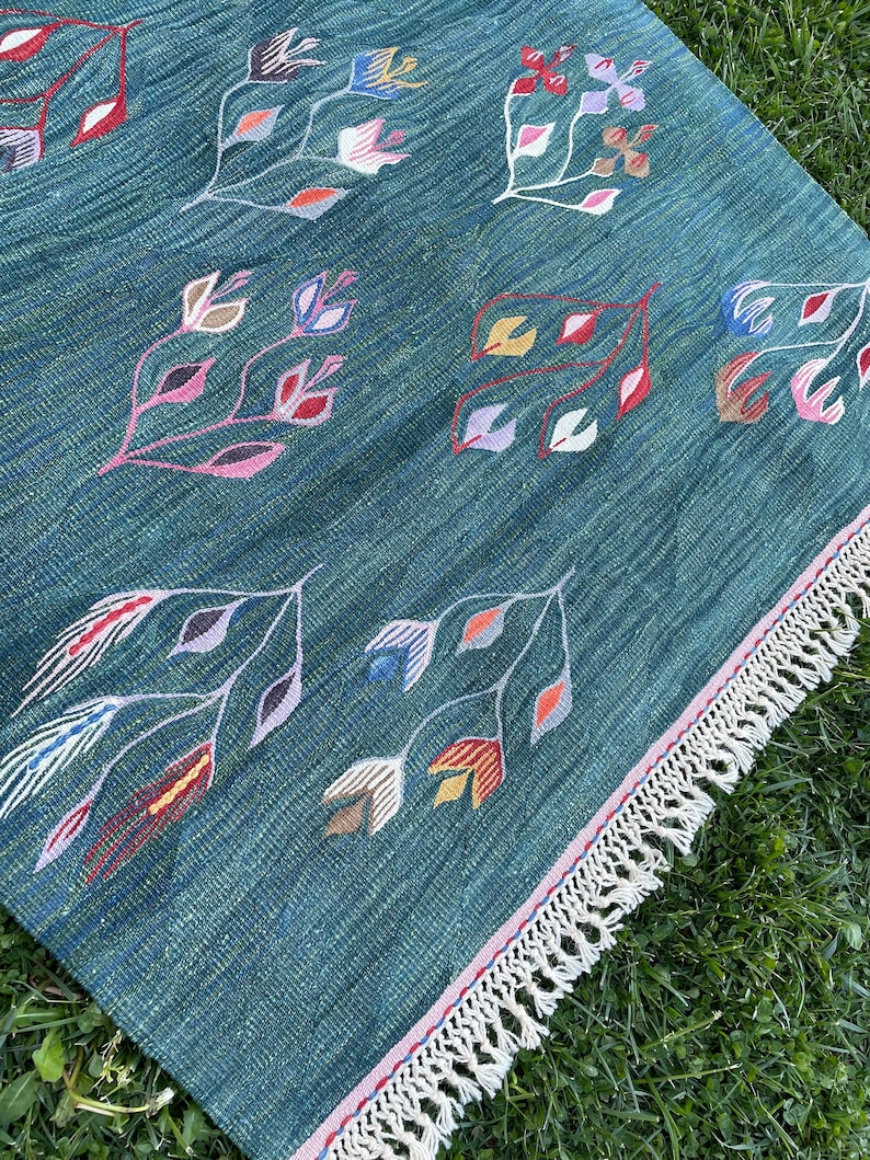 May include: A teal blue rug with a fringe border. The rug has a repeating pattern of stylized flowers in shades of pink, red, yellow, blue, and green.