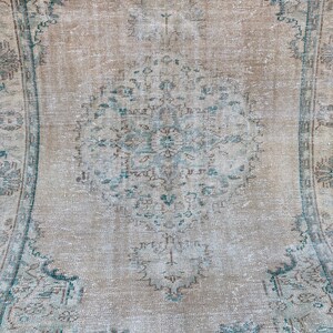 May include: A vintage rug with a faded, light brown background and a central design featuring intricate blue and brown floral patterns. The rug has a distressed, worn look, adding to its vintage charm.