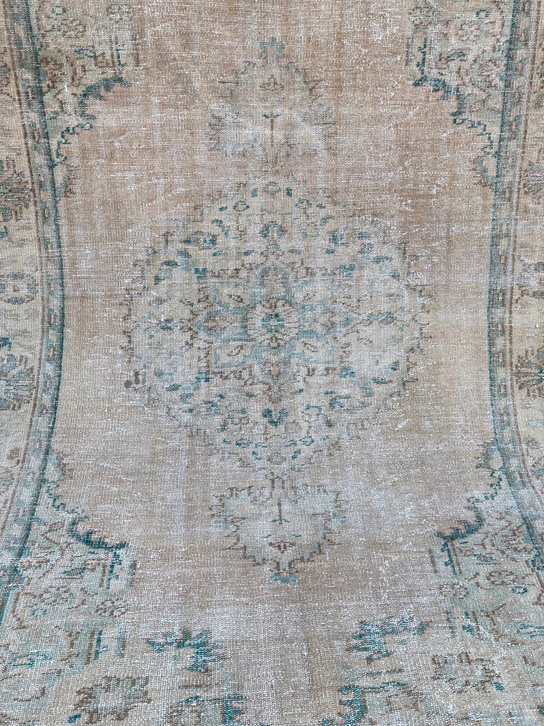 May include: A vintage rug with a faded, light brown background and a central design featuring intricate blue and brown floral patterns. The rug has a distressed, worn look, adding to its vintage charm.