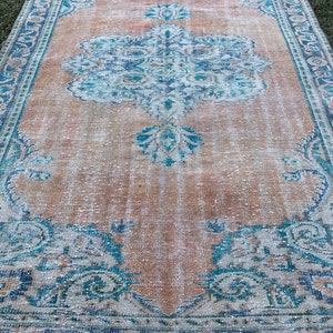 May include: A vintage rug with a faded peach background and a blue and white floral pattern. The rug has a distressed look and is perfect for adding a touch of bohemian style to any room.