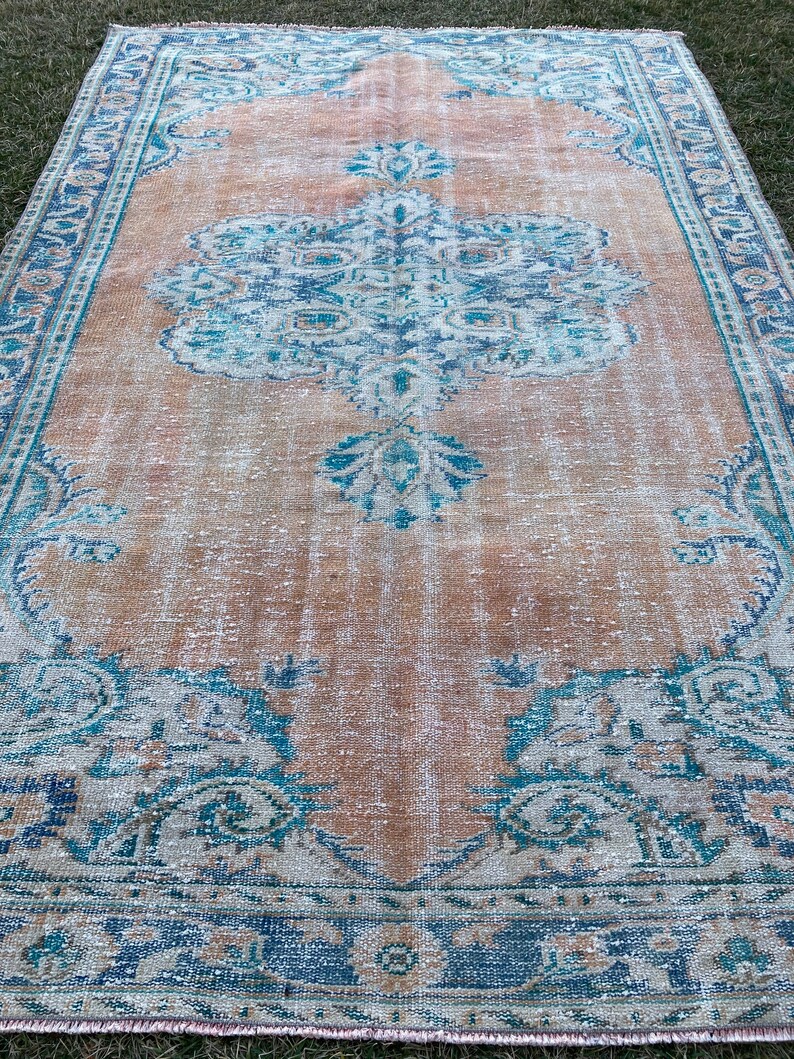 May include: A vintage rug with a faded peach background and a blue and white floral pattern. The rug has a distressed look and is perfect for adding a touch of bohemian style to any room.