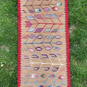 May include: A long, narrow rug with a brown background and a repeating pattern of stylized trees with colorful leaves. The rug has a red border with white fringe.