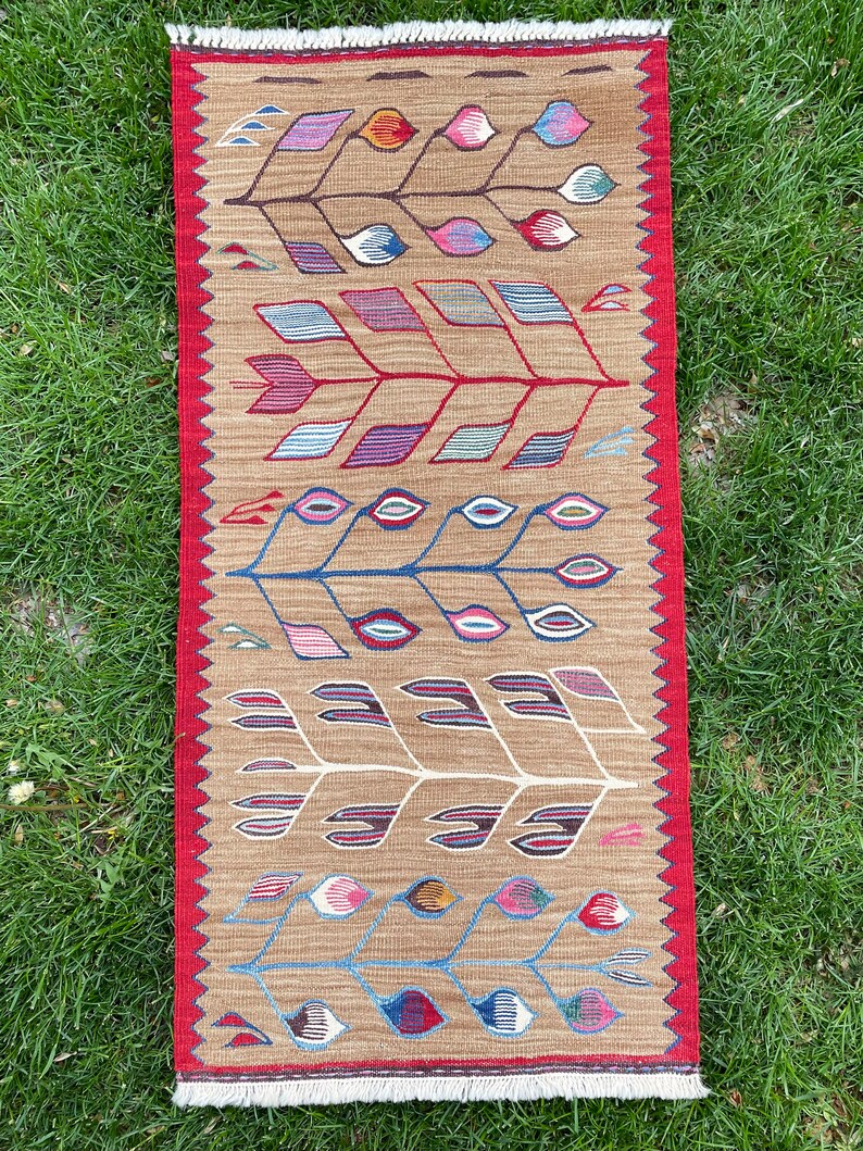May include: A long, narrow rug with a brown background and a repeating pattern of stylized trees with colorful leaves. The rug has a red border with white fringe.