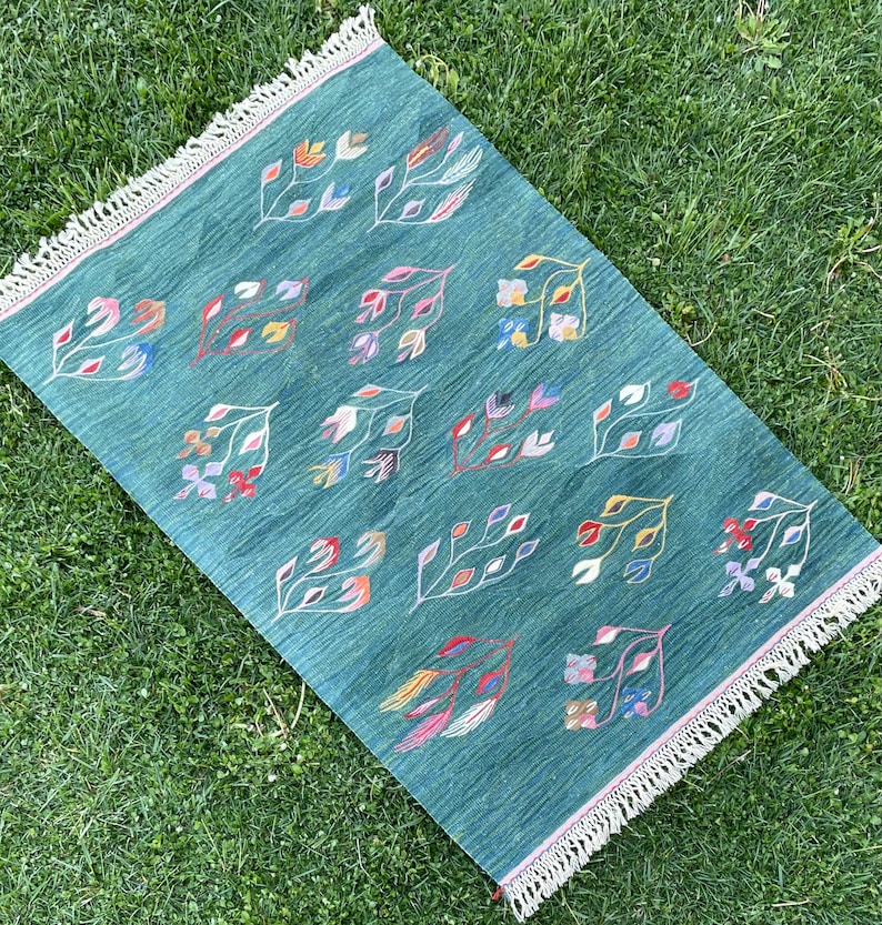 May include: A teal blue rug with a fringe border features a repeating pattern of colorful stylized floral designs.