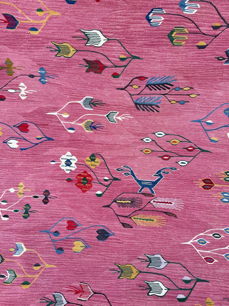 May include: A pink rug with a repeating pattern of stylized flowers and leaves in shades of blue, red, yellow, and white.