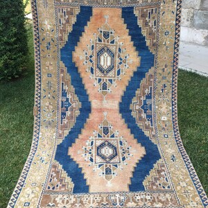 May include: A vintage rug with a blue and peach geometric pattern. The rug has a fringed border and is made of wool.