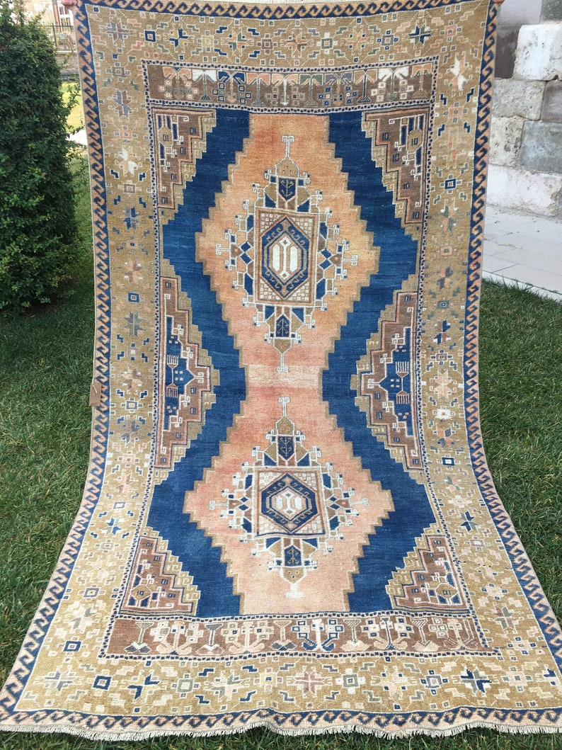 May include: A vintage rug with a blue and peach geometric pattern. The rug has a fringed border and is made of wool.