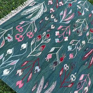 May include: A teal blue rug with a floral pattern. The rug has a fringe border and features white, pink, and red flowers.