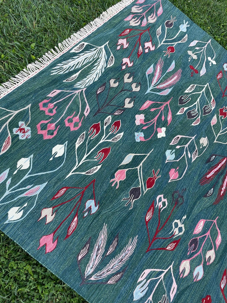 May include: A teal blue rug with a floral pattern. The rug has a fringe border and features white, pink, and red flowers.