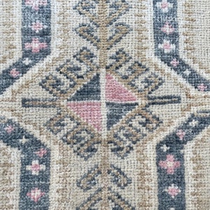Puede incluir: Primer plano de una alfombra beige con un patr&oacute;n geom&eacute;trico en tonos grises, rosa y marr&oacute;n. El patr&oacute;n presenta una forma de diamante central con diamantes m&aacute;s peque&ntilde;os y motivos florales.