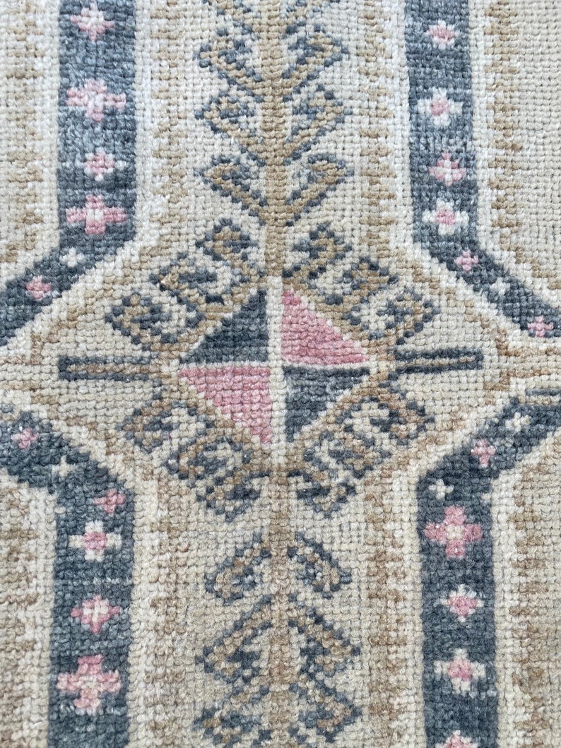 Puede incluir: Primer plano de una alfombra beige con un patr&oacute;n geom&eacute;trico en tonos grises, rosa y marr&oacute;n. El patr&oacute;n presenta una forma de diamante central con diamantes m&aacute;s peque&ntilde;os y motivos florales.