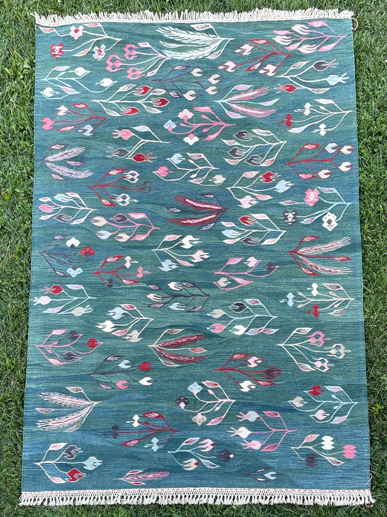 May include: A teal blue rug with a floral pattern. The rug features white, pink, and red stylized flowers and leaves.