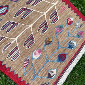 May include: A brown rug with a white, blue, and red floral pattern. The rug has a red border with a white fringe.