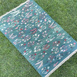 May include: A teal blue rug with a floral pattern in shades of pink and green. The rug has a fringe border.