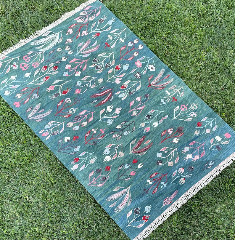 May include: A teal blue rug with a floral pattern in shades of pink and green. The rug has a fringe border.