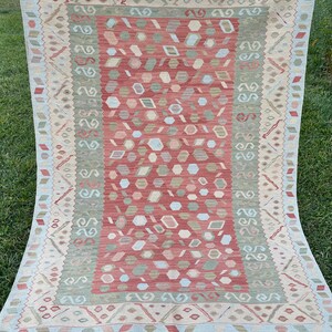 K&ouml;nnte beinhalten: Ein traditioneller Teppich in Rot-, Gr&uuml;n- und Cremet&ouml;nen. Der Teppich hat ein geometrisches Muster mit einem zentralen Medaillon und einem Rand.