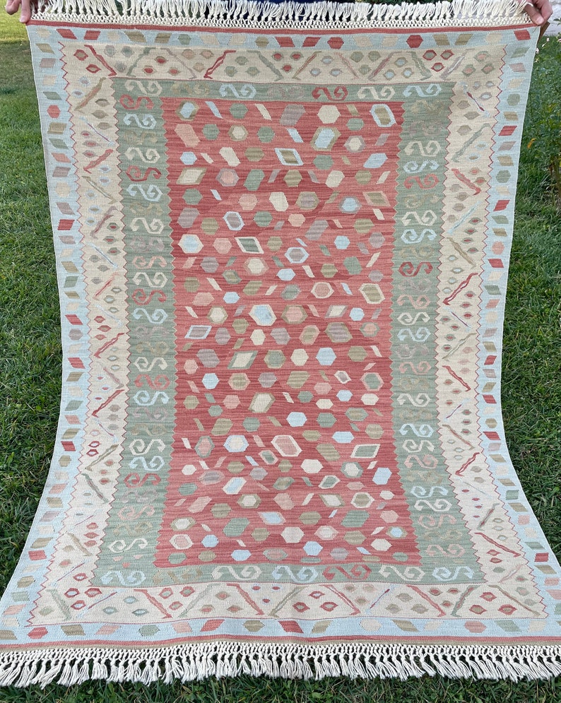 K&ouml;nnte beinhalten: Ein traditioneller Teppich in Rot-, Gr&uuml;n- und Cremet&ouml;nen. Der Teppich hat ein geometrisches Muster mit einem zentralen Medaillon und einem Rand.