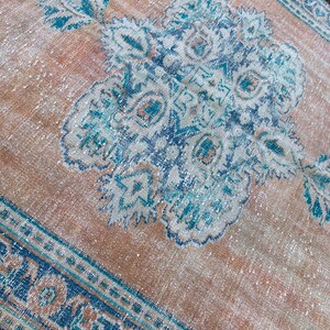 May include: A vintage rug with a faded peach background and a blue and white floral pattern. The rug has a border with a geometric design.