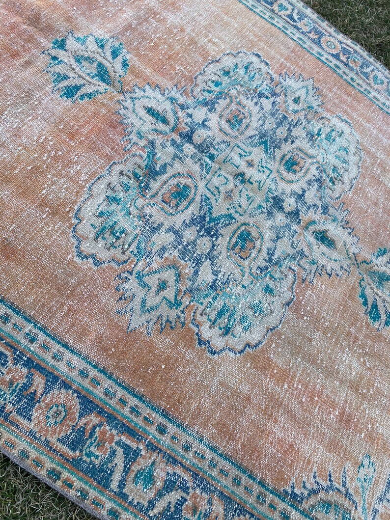 May include: A vintage rug with a faded peach background and a blue and white floral pattern. The rug has a border with a geometric design.