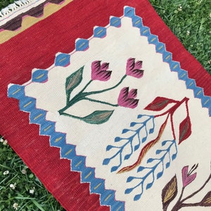 May include: A white and red rug with a floral design. The rug has a blue and gold border. The rug is made of wool and is hand-woven.
