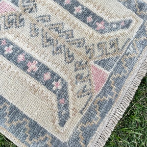 Puede incluir: Una alfombra de color crema con un patr&oacute;n geom&eacute;trico azul y rosa. La alfombra tiene un borde de flecos.
